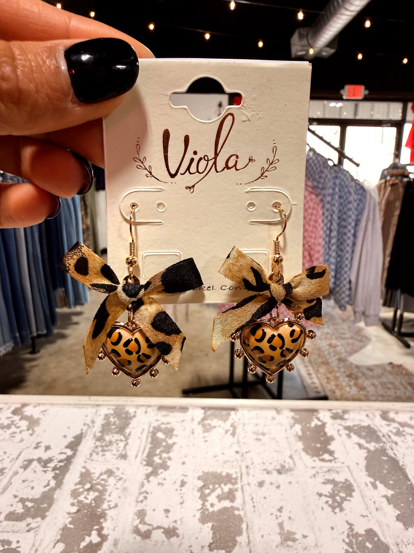 Leopard print heart earrings on a 'Viola' branded card with clothing store background