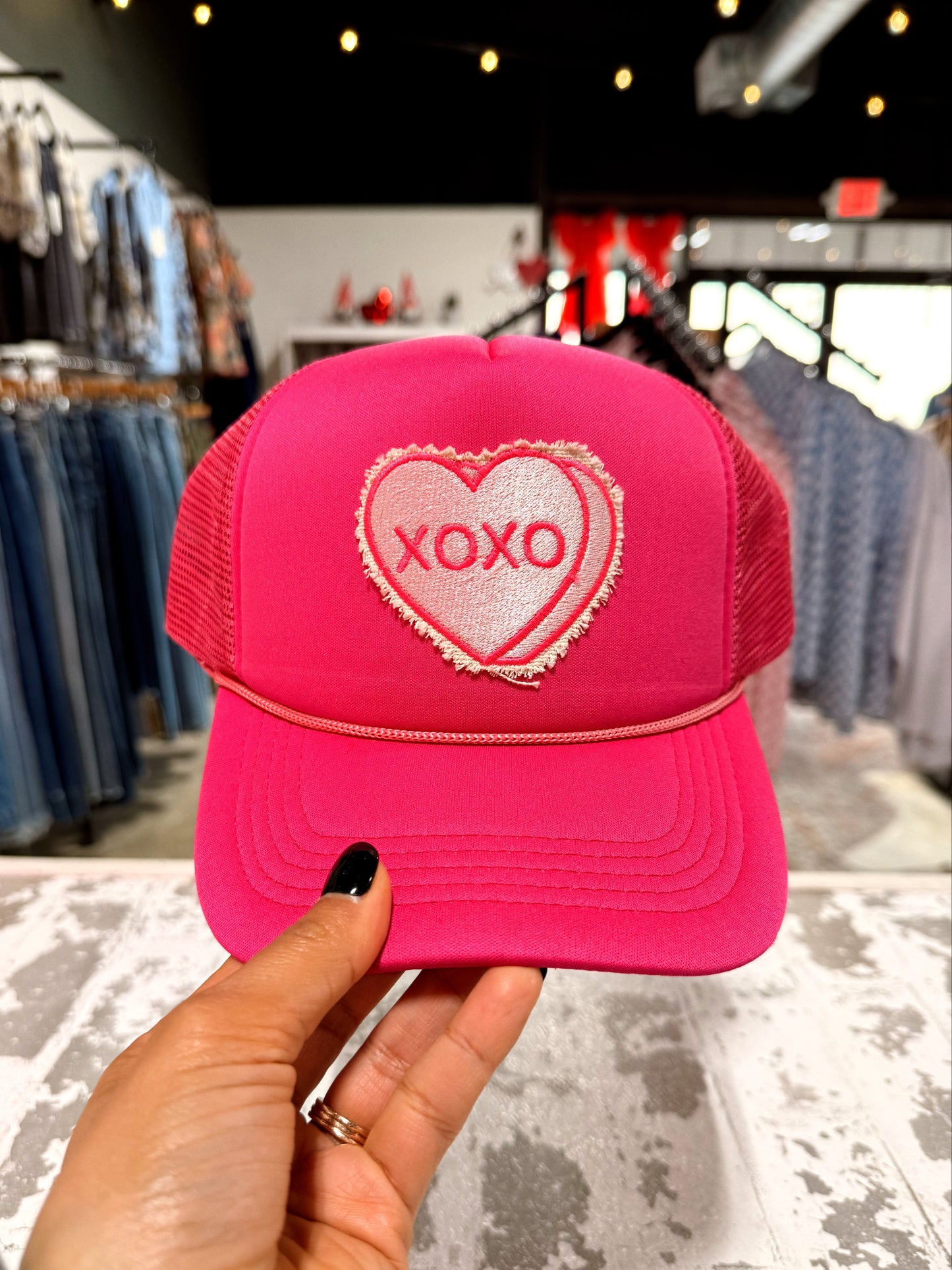 Pink cap with heart and 'XOXO' design held in front of a store interior.