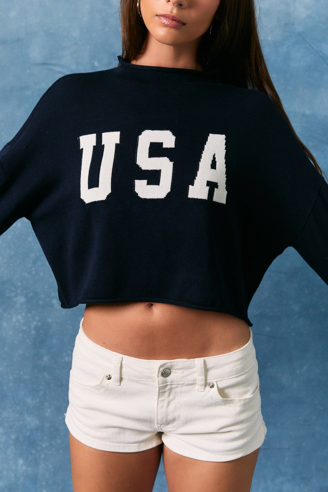 Woman wearing a navy cropped mock neck sweater with white USA lettering and long sleeves. 🤍🇺🇸