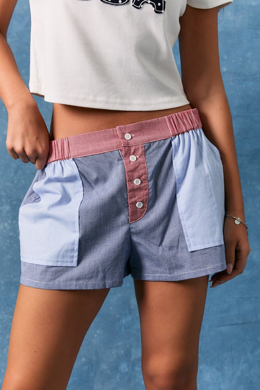 Women's blue gingham boxer shorts featuring a pink contrast elastic waistband, button-front detail, and oversized patch pockets.