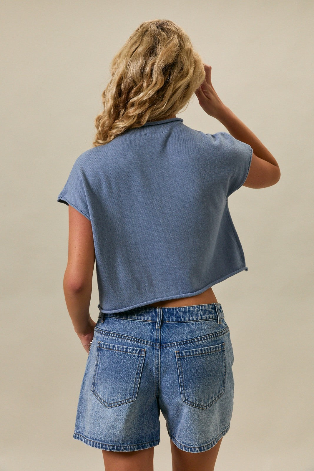 Woman wearing a blue mock neck sweater with an American flag graphic and relaxed drop shoulder silhouette.