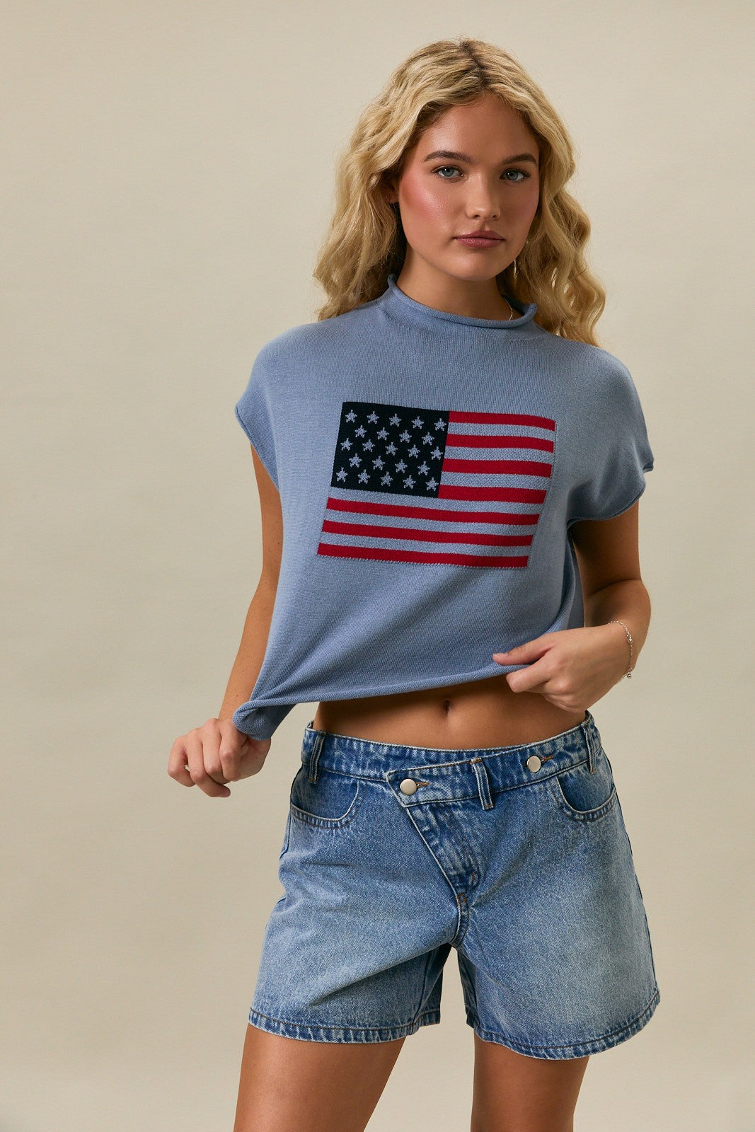 Woman wearing a blue mock neck sweater with an American flag graphic and relaxed drop shoulder silhouette.