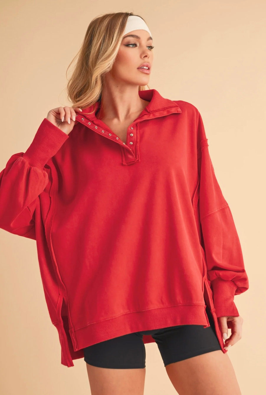 Woman wearing a red oversized henley on a beige background
