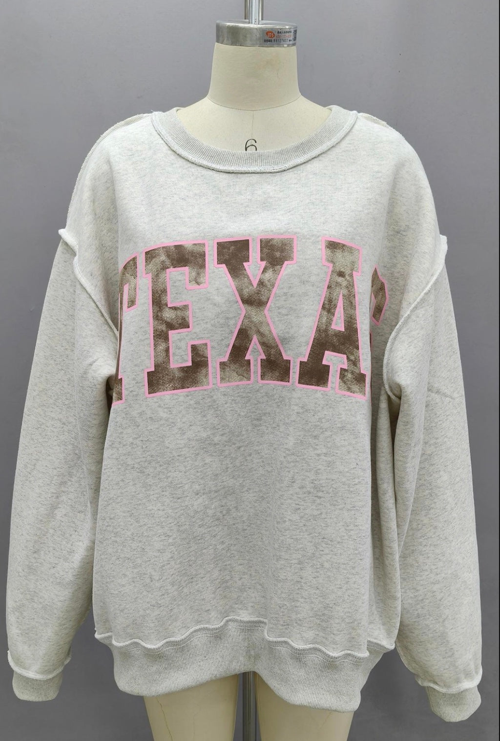 Gray sweatshirt with 'TEXAS' camo print on a mannequin against a gray background