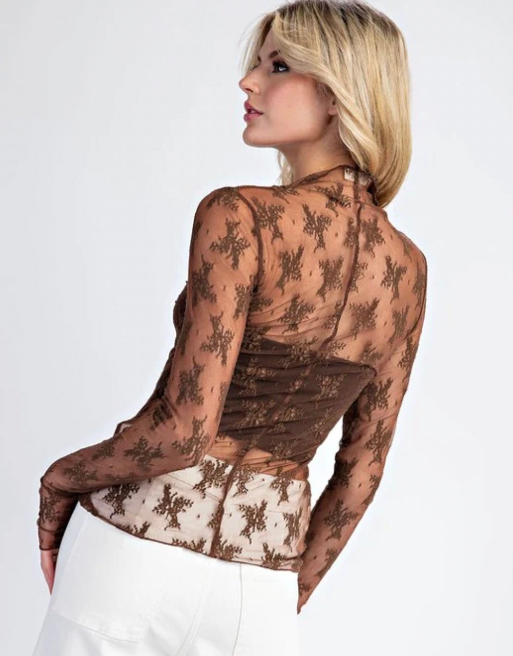 Woman wearing a sheer lace top with a plain background