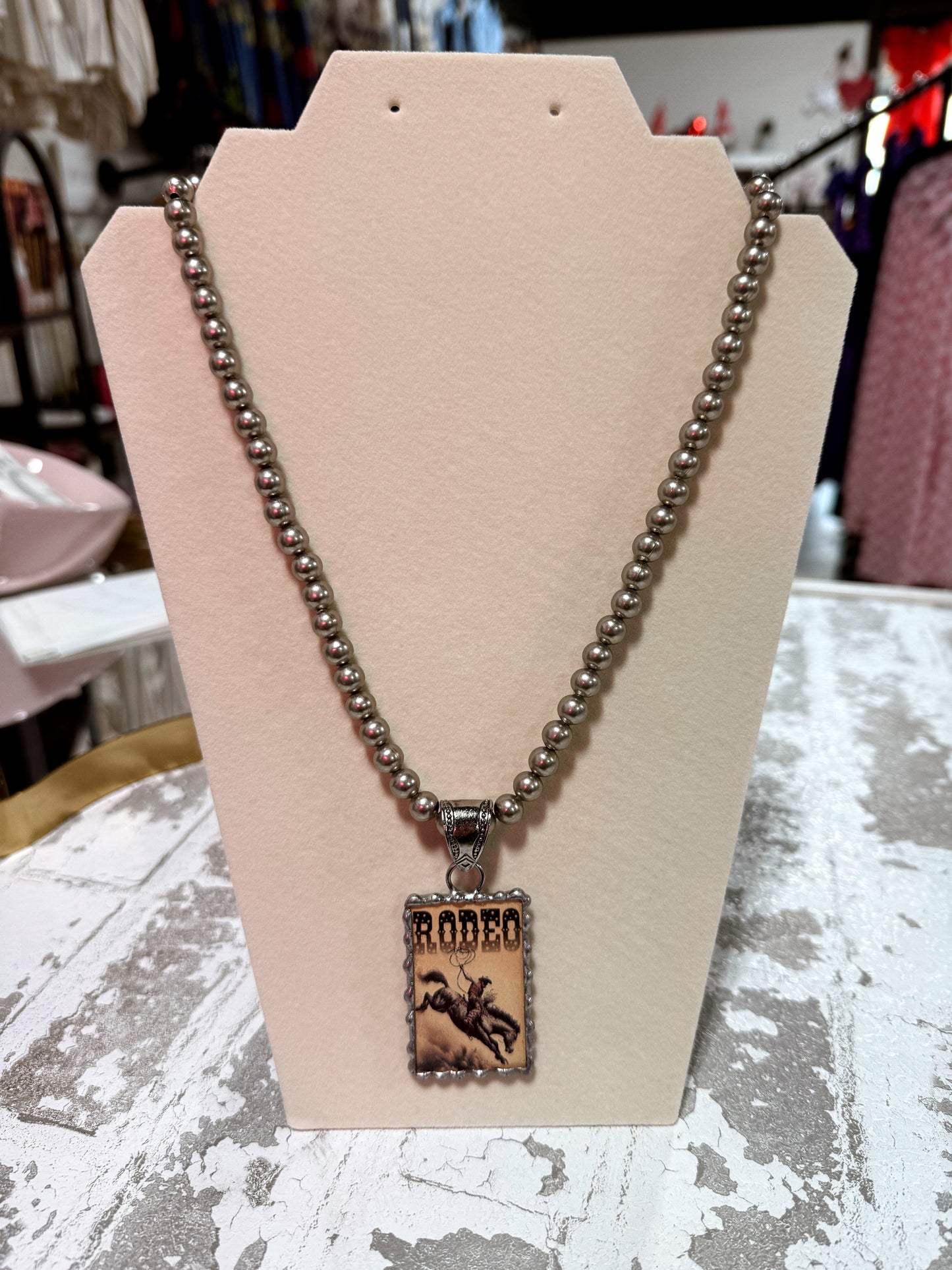 Necklace with a 'Rodeo' pendant on a beige display stand.