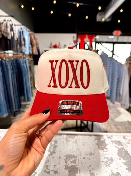 Red and white cap with 'XOXO' text held in a store setting