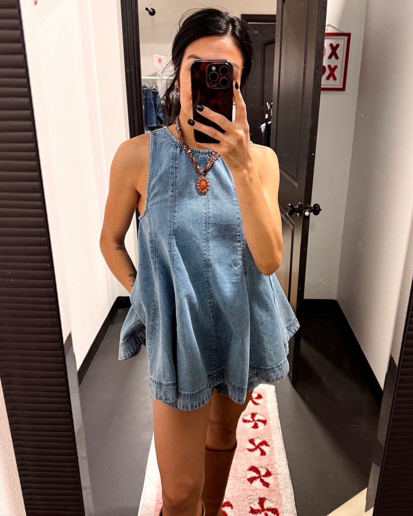 Person wearing a denim dress taking a mirror selfie in a fitting room.