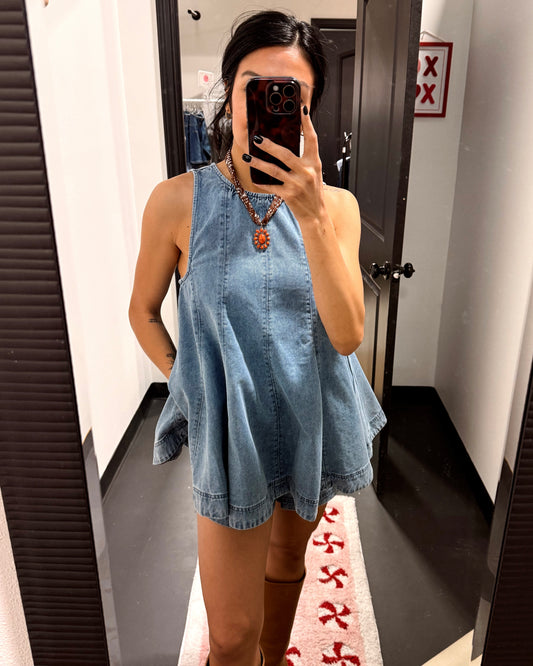 Person wearing a denim dress taking a mirror selfie in a fitting room.