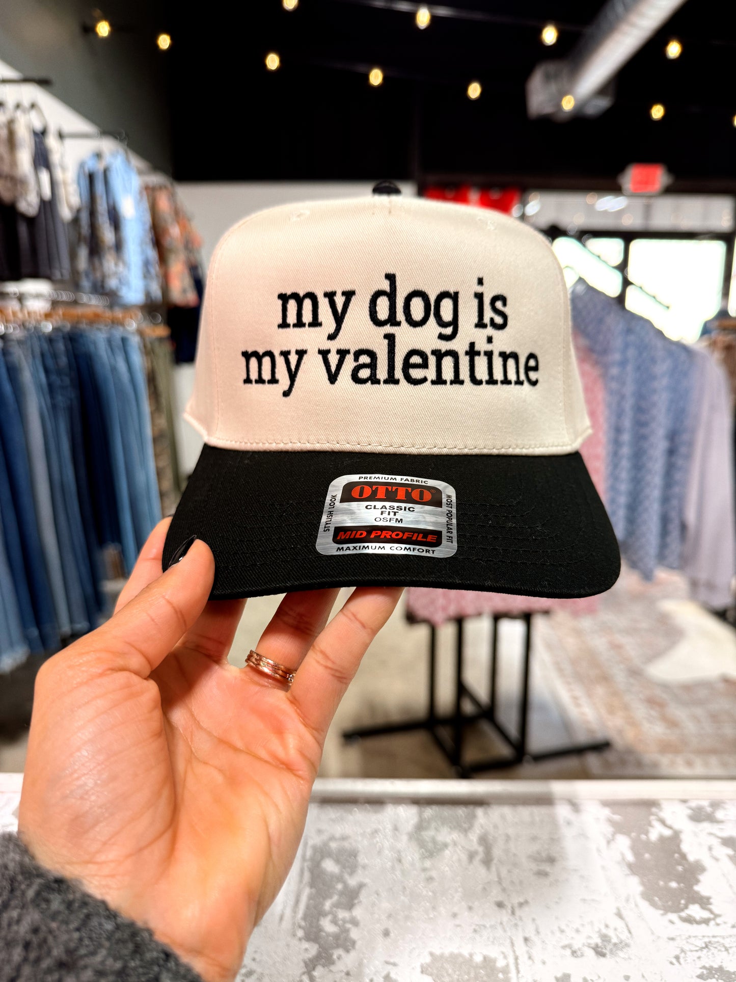 Cap with 'my dog is my valentine' text held in a hand, with store interior in the background.