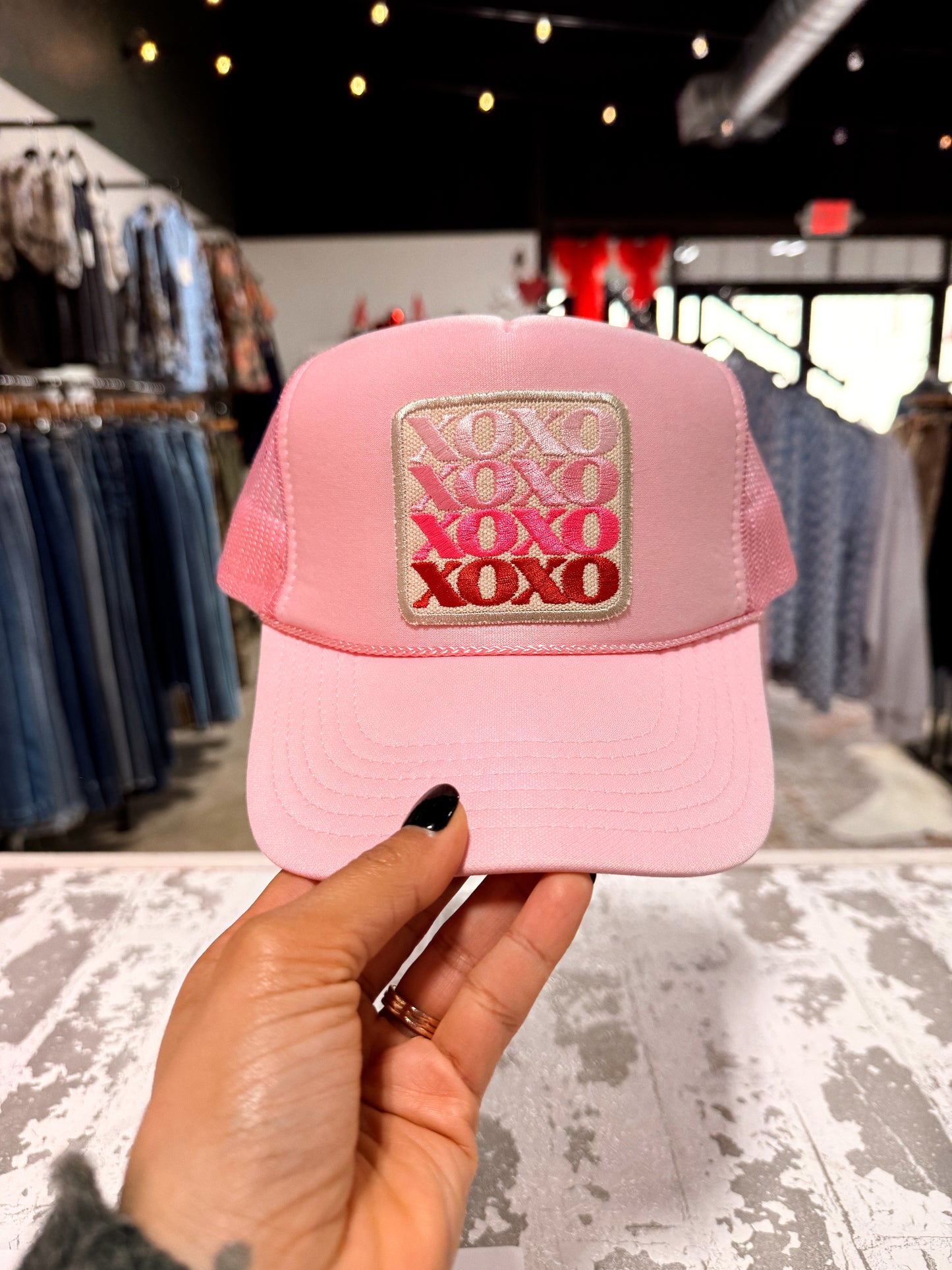 Pink cap with 'XOXO' patch held in a store setting