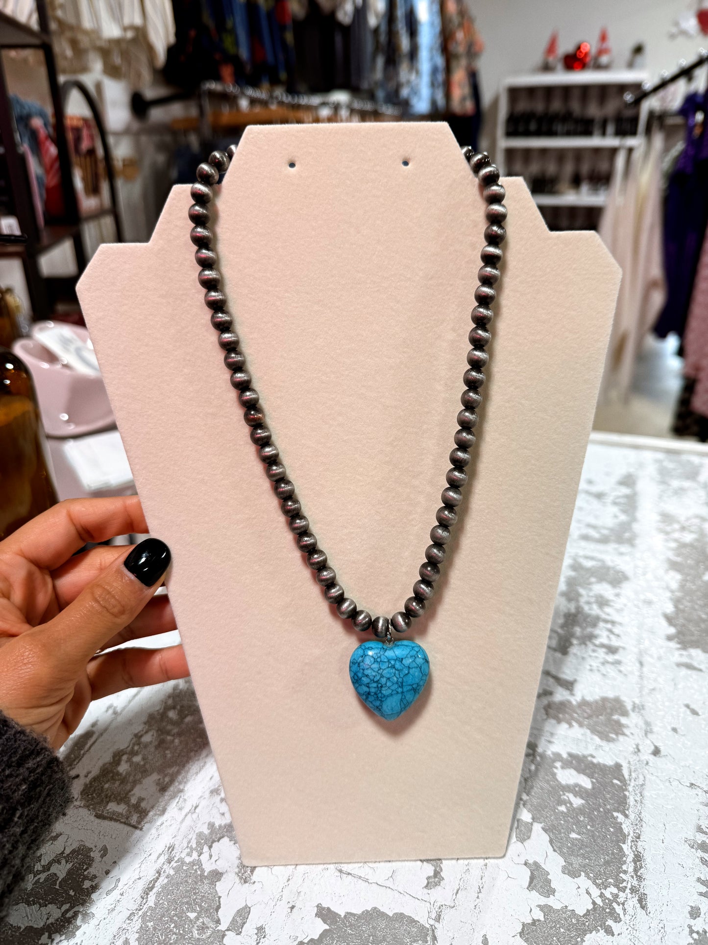 Necklace with a blue heart pendant on a beige display card, held by a person.