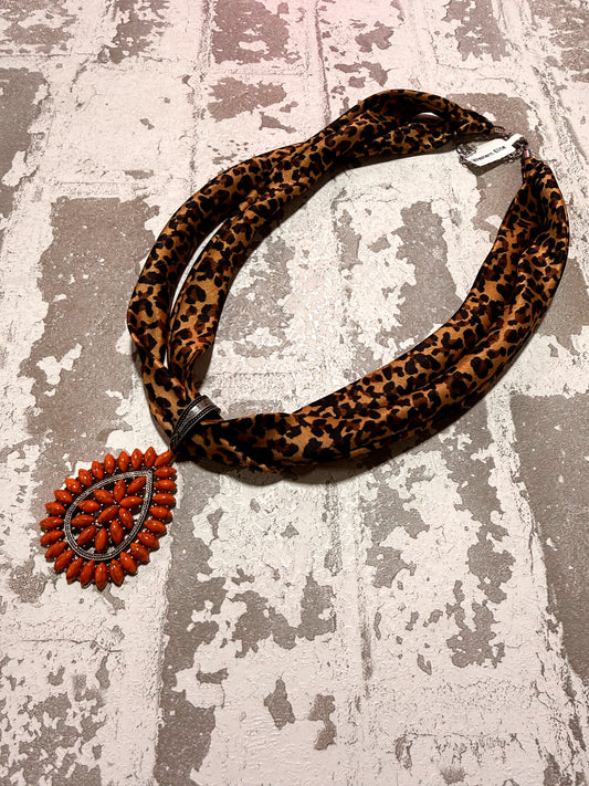 Leopard print necklace with a decorative orange pendant on a textured surface