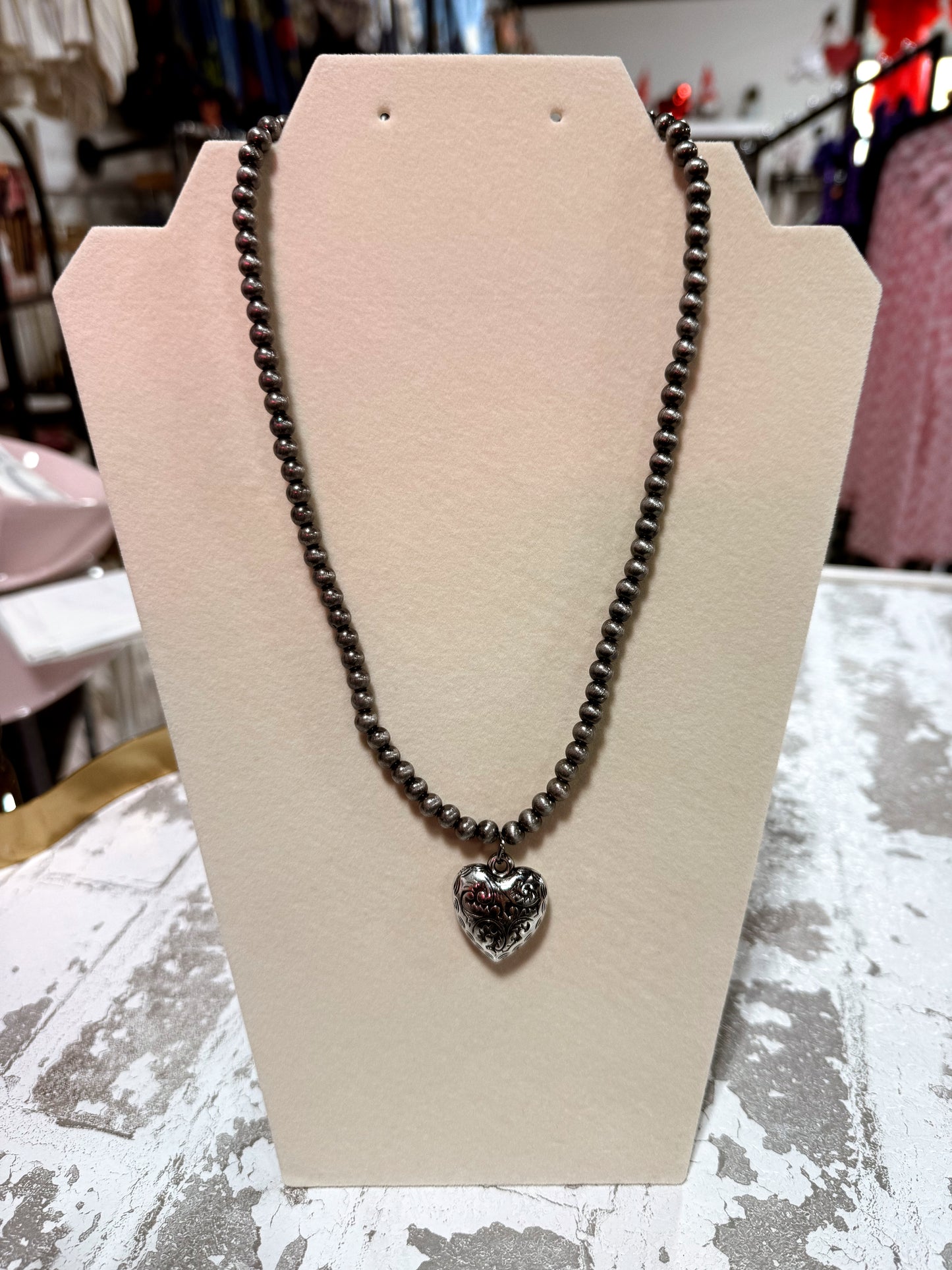 Necklace with a heart-shaped pendant on a beige stand against a blurred background