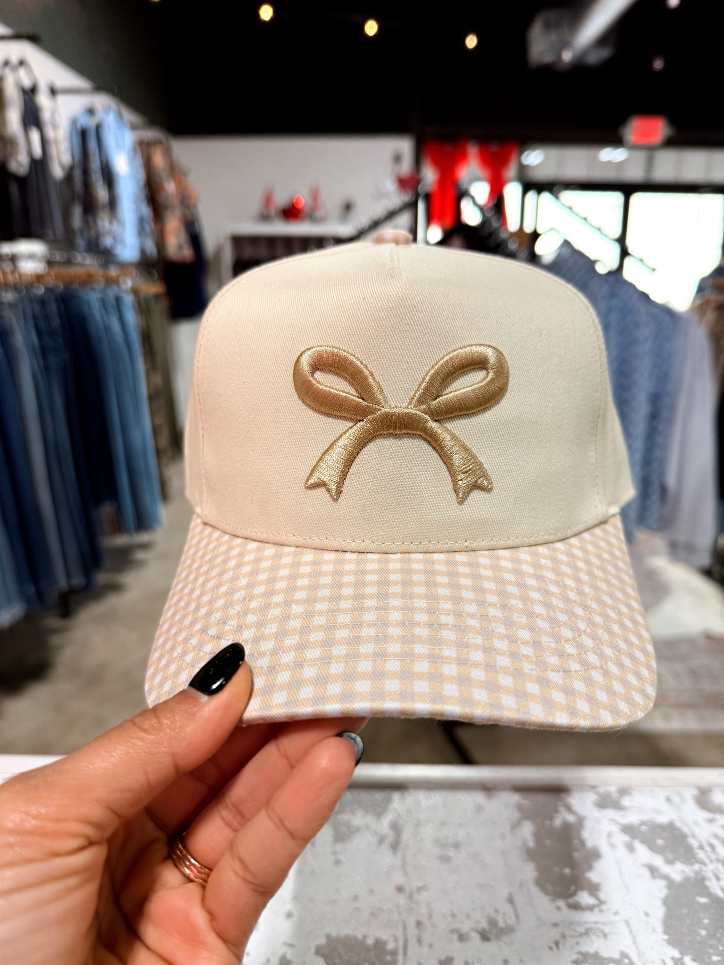Beige cap with a bow design held by a hand in a store setting
