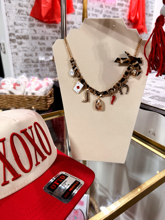 Necklace with charms on a mannequin bust next to a red cap with 'XOXO' text in a store setting.