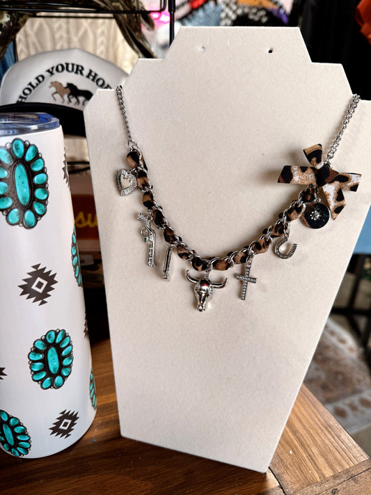Necklace with leopard print and metallic charms on a white stand next to a tumbler with turquoise designs.